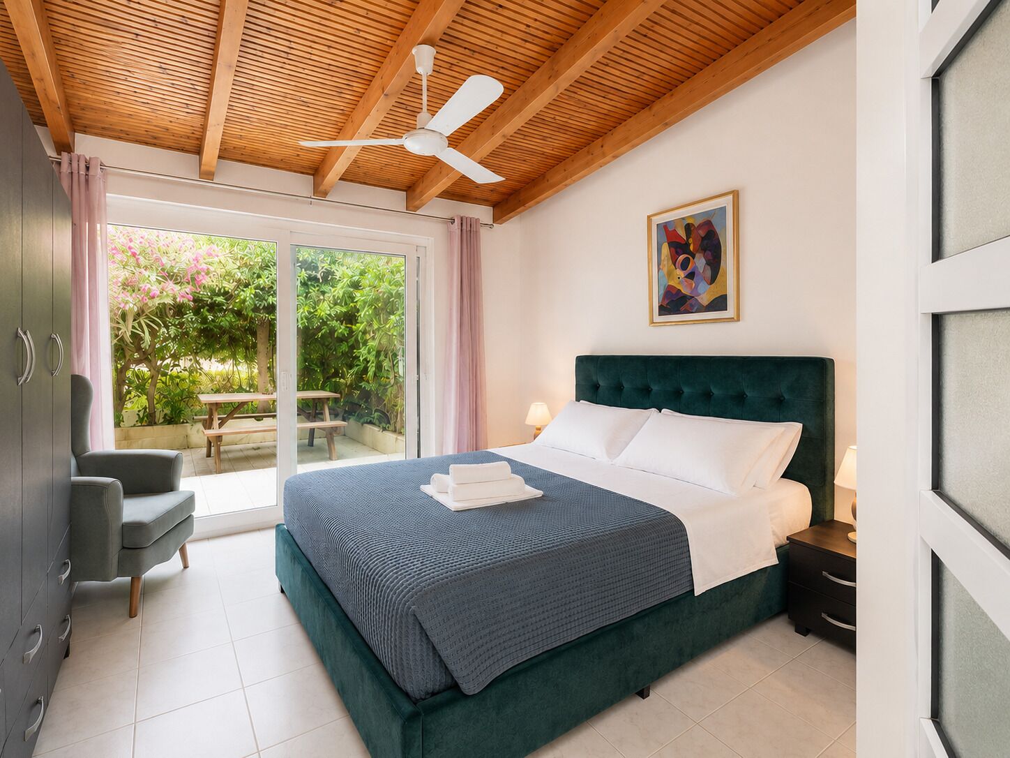 Une chambre à coucher avec un lit, un bureau et une chaise. Il y a une fenêtre avec des rideaux et une vue sur la verdure à l’extérieur.