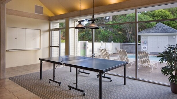 A ping pong table in a room with large windows, a whiteboard, and outdoor seating by a pool. - WM BLOCK Gleneden - 1br (Lincoln Beach)