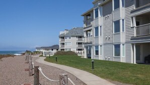 A beachfront residential building with multiple balconies, a paved walkway, and a clear view of the ocean. - WM BLOCK Gleneden - 1br (Lincoln Beach)