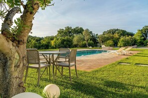 Ein Poolbereich mit Tisch und Stühlen, umgeben von Gras und Bäumen.