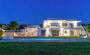 Une maison moderne à deux étages, dotée d’une piscine, d’un espace salon extérieur et d’un mur en pierre.