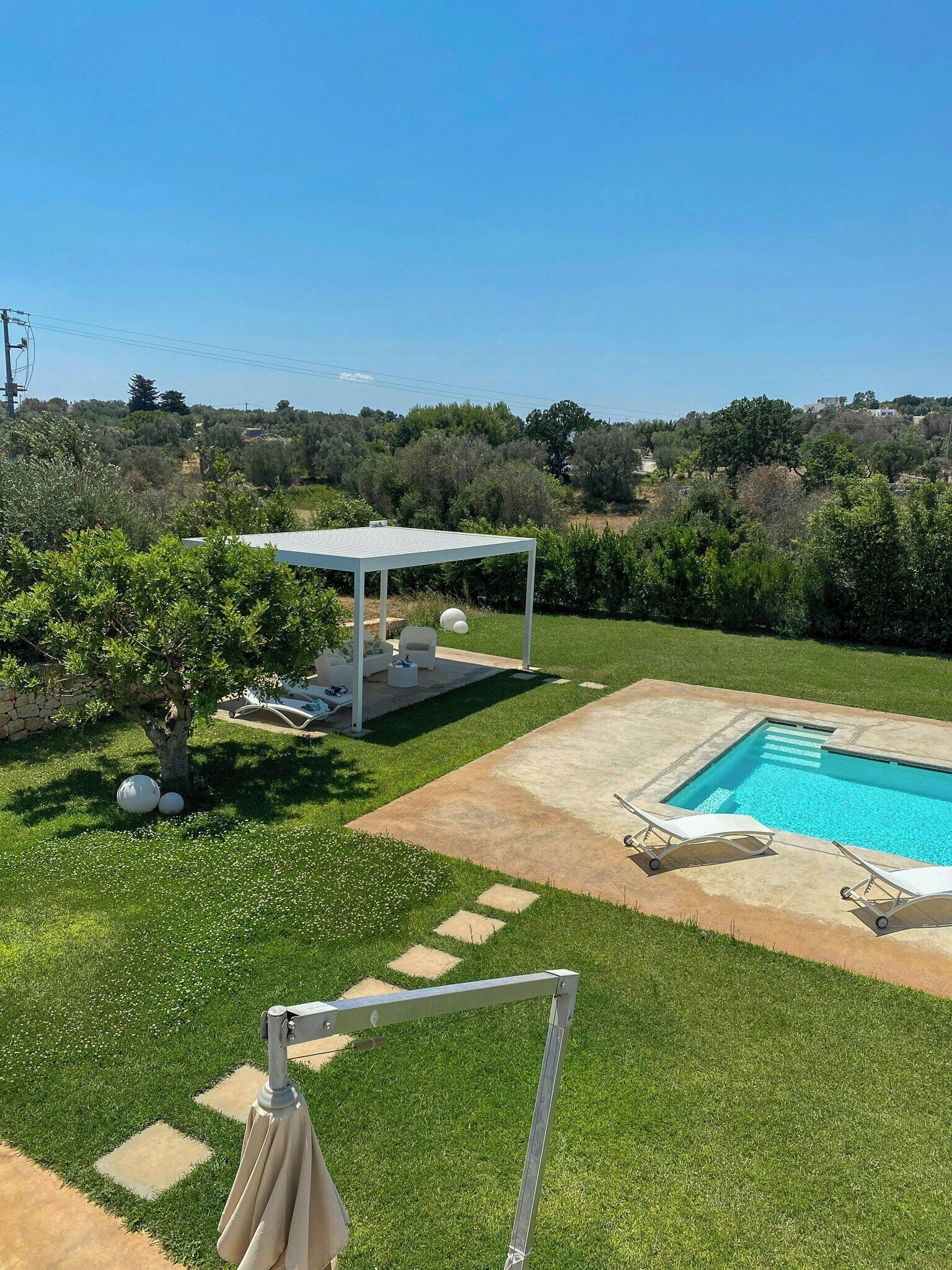 Un jardin avec une piscine, un espace salon couvert et une pelouse.