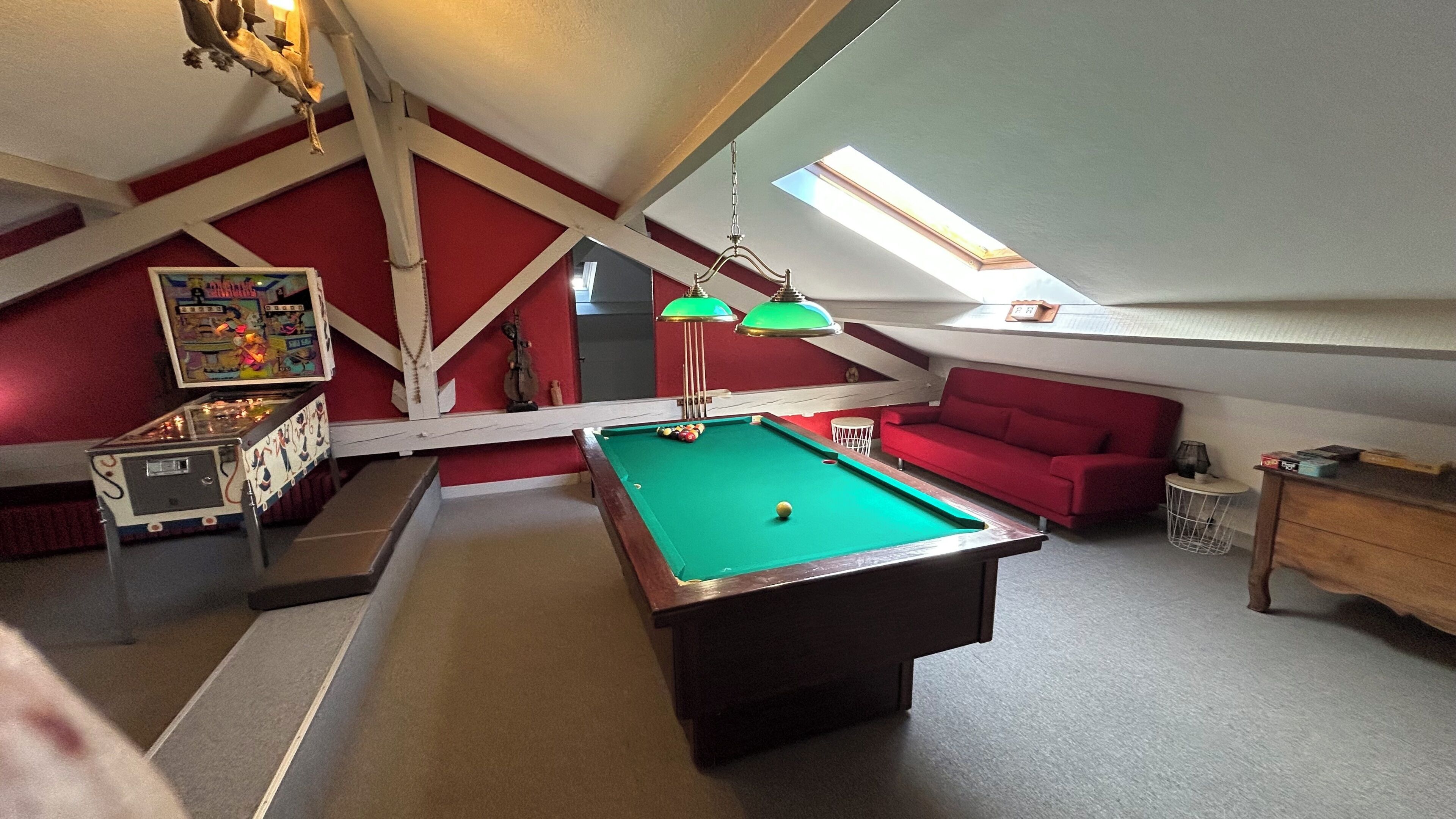 Quarto com mesa de bilhar, paredes vermelhas, sofá vermelho e teto com claraboias.