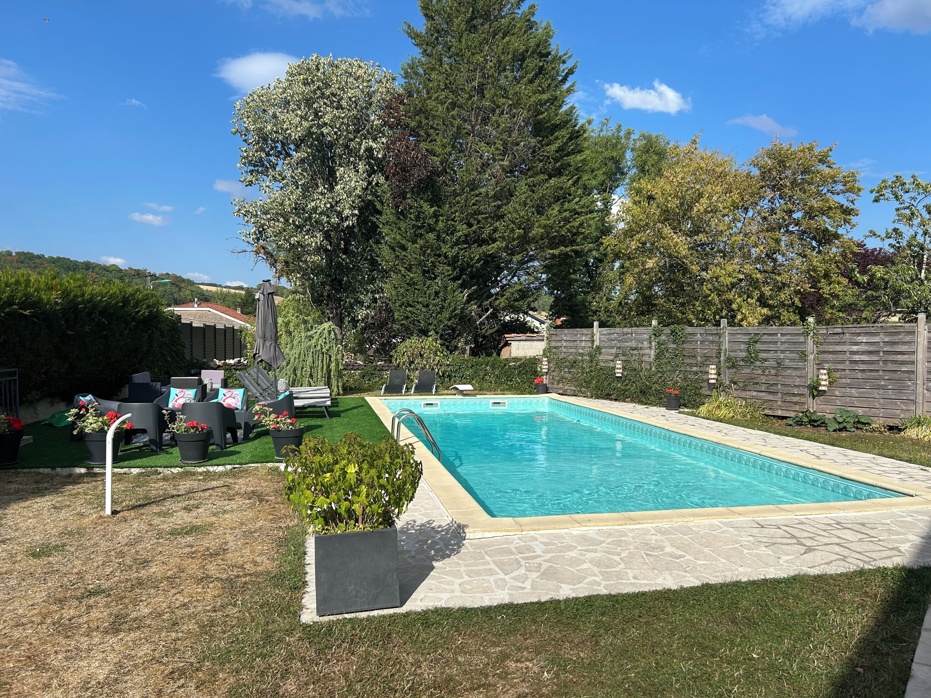 Piscina rectangular con borde de piedra, rodeada por césped y una cerca de madera.