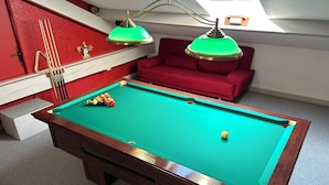 A pool table with a green felt surface, surrounded by a red sofa and a staircase. - VILLA NORA: HOUSE WITH A SWIMMING POOL IN DEMANGE-AUX-EAUX (DEMANGE BAUDIGNECOURT)
