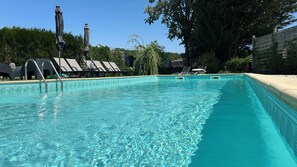 A clear swimming pool with lounge chairs and umbrellas.