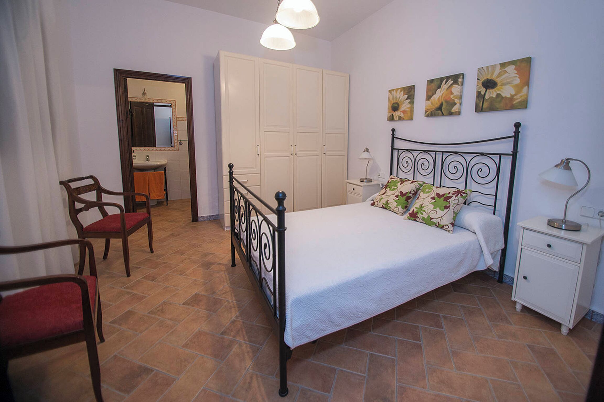 Um quarto com uma cama, uma cadeira, uma mesinha de cabeceira, um abajur e um guarda-roupa.