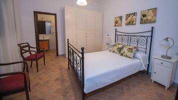 Um quarto com uma cama, uma cadeira, uma mesinha de cabeceira, um abajur e um guarda-roupa.
