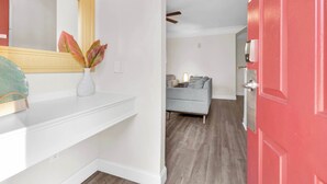 A hallway with a white wall, a red door, a grey sofa, and a white console table with a vase of flowers. - Runaway Beach Club Disney Retreat (Kissimmee)