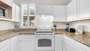 A modern kitchen with white cabinetry, a built-in microwave, a stove, and a coffee maker. - Runaway Beach Club Disney Retreat (Kissimmee)