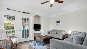A living room with a grey sofa, a wooden coffee table, a television on a stand, and a ceiling fan. - Runaway Beach Club Disney Retreat (Kissimmee)
