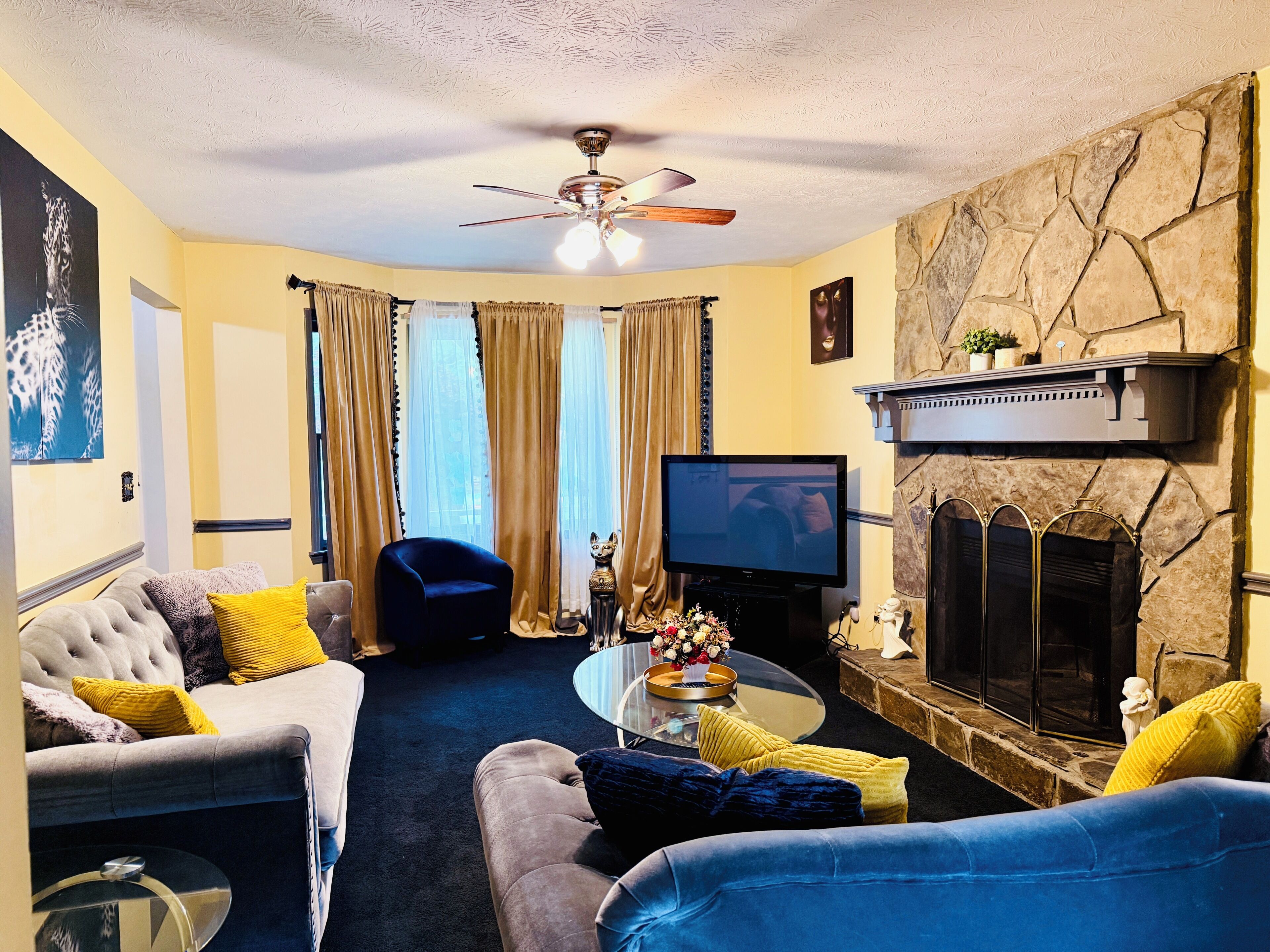 A living room with a fireplace, a television, and a ceiling fan.
