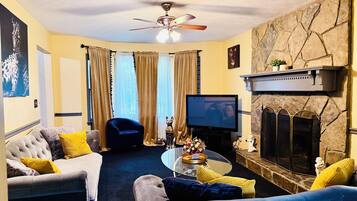 A living room with a fireplace, a television, and a ceiling fan.