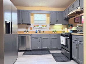 A modern kitchen with grey cabinets, stainless steel appliances, and a window with flower boxes.