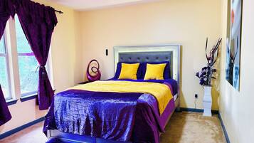 A bedroom with a bed, curtains, a vase with flowers, and a ceiling fan.