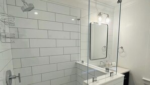 Et moderne badeværelse med hvide metrofliser, et glasbadeværelsesafskærmning, en hvid vask med spejl og gulv med sekskantede fliser.