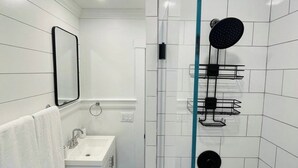 Et moderne badeværelse med en glas brusekabine, en hvid vask og et spejl.