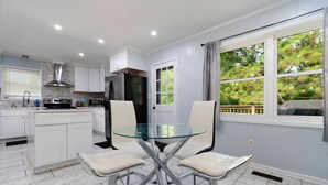 A modern kitchen with white cabinets, a stainless steel refrigerator, and a glass dining table with four chairs. - Perfect 3-bedroom house with AC in welcoming Birmingham. (Birmingham)
