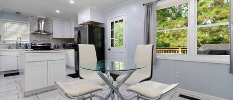 A modern kitchen with white cabinets, a stainless steel refrigerator, and a glass dining table with four chairs.
