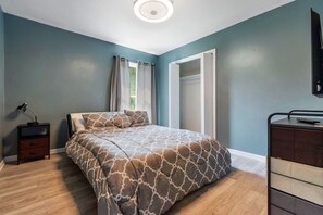 Quarto com cama, mesa de cabeceira, cômoda, janela com cortinas e luminária no teto.