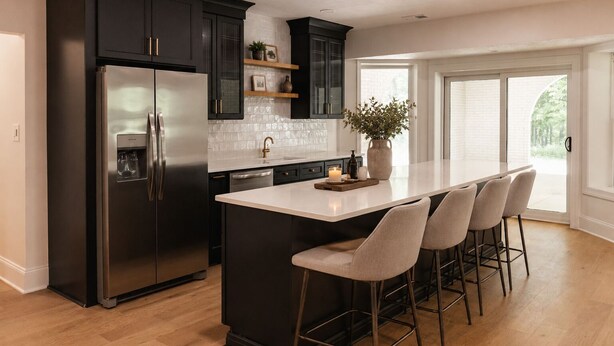 A modern kitchen with a stainless steel refrigerator, dark cabinetry, a white island with bar stools, and a large window providing natural light. - Luxury Estate Weddings • Retreats • Group Stays (Akron)