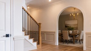 A staircase with a wooden handrail and black balusters leading to a dining area with a chandelier. - Luxury Estate Weddings • Retreats • Group Stays (Akron)