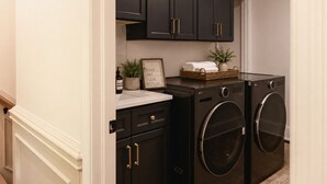 A laundry room with two black washing machines, a sink, and a basket with towels. - Luxury Estate Weddings • Retreats • Group Stays (Akron)