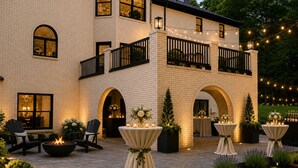 A two-story building with a brick facade, outdoor seating area with tables and chairs, and string lights. - Luxury Estate Weddings • Retreats • Group Stays (Akron)