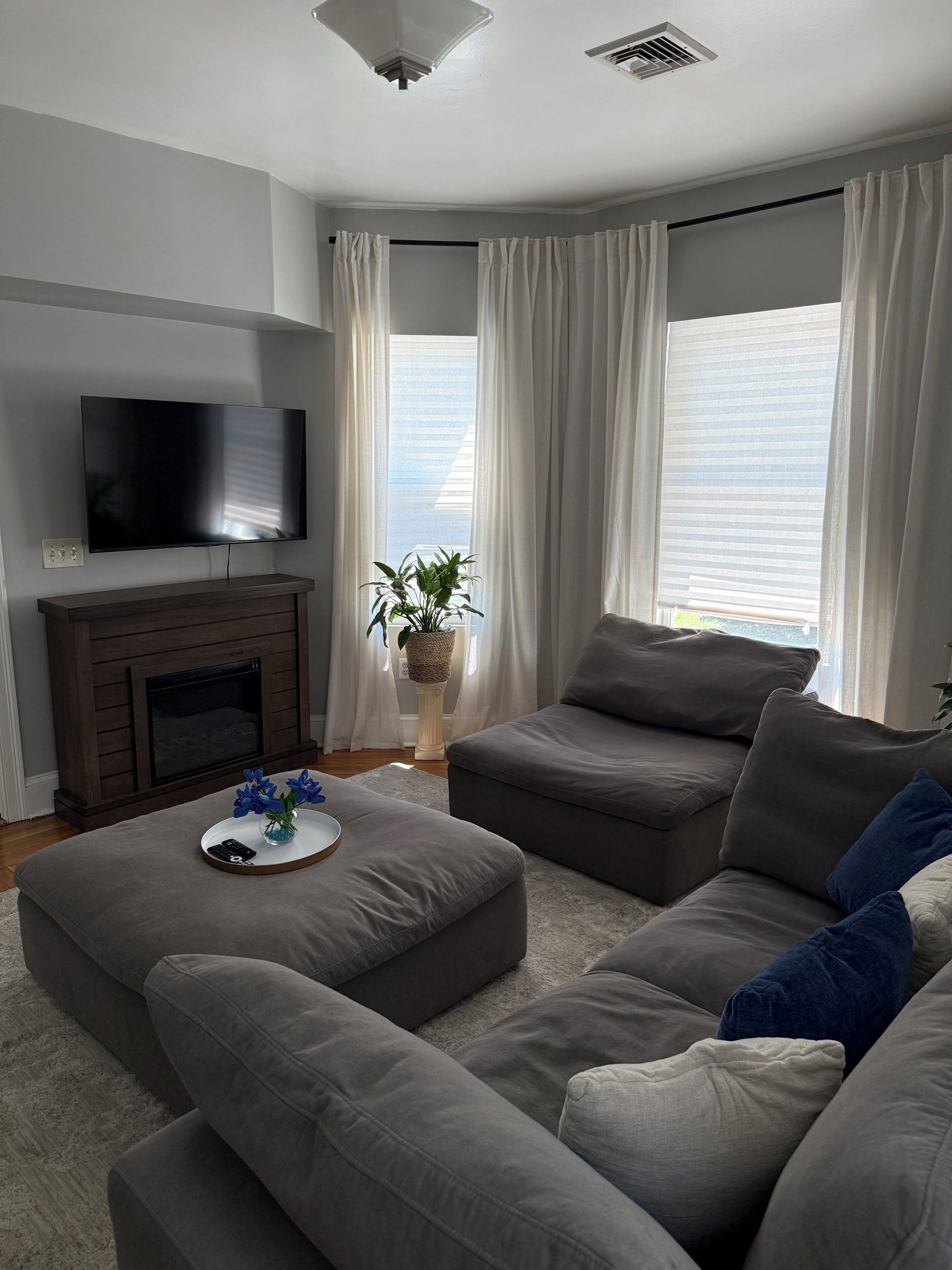 A modern living room with a flat-screen TV, a fireplace, and a large window with curtains.