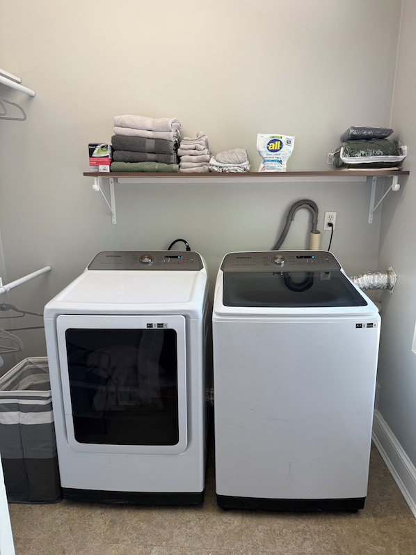 Two white front-loading washers with a shelf above containing folded towels and a cleaning product.