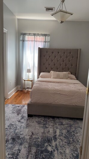 A bedroom with a large bed, a bedside table, a lamp, and a window with curtains.