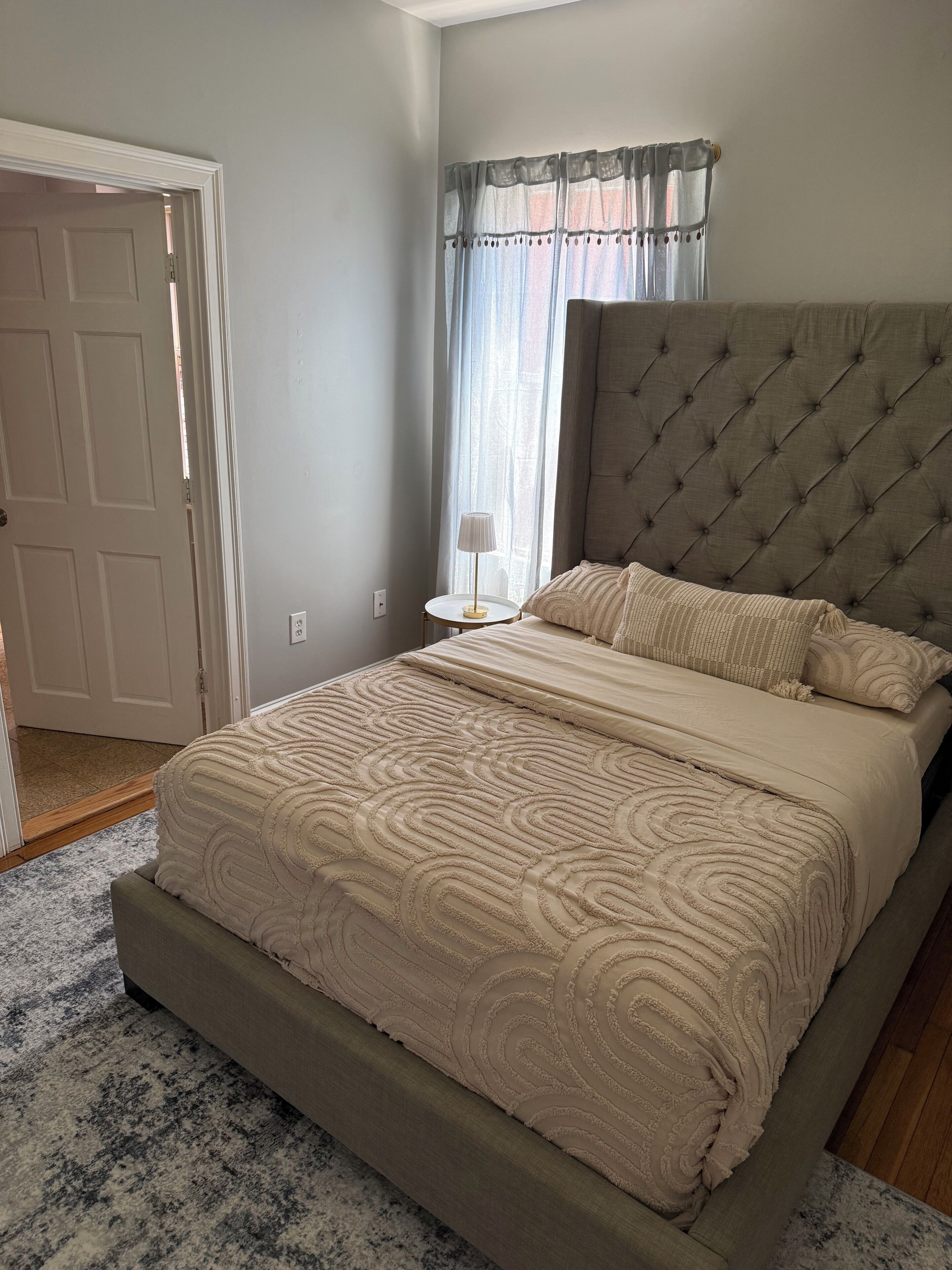 A bedroom with a large bed, a nightstand, a lamp, and a window with curtains.