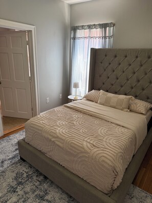 Une chambre à coucher avec un grand lit, une table de chevet, une lampe et une fenêtre avec des rideaux.
