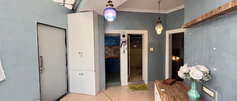 A room with a bed, a wardrobe, a desk with a vase of flowers, and a ceiling light fixture.
