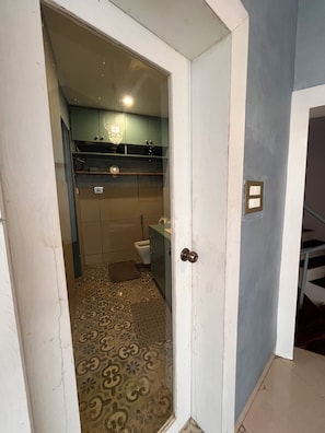 Un couloir étroit mène à une salle de bain équipée de toilettes, d’un lavabo et d’un meuble de rangement.