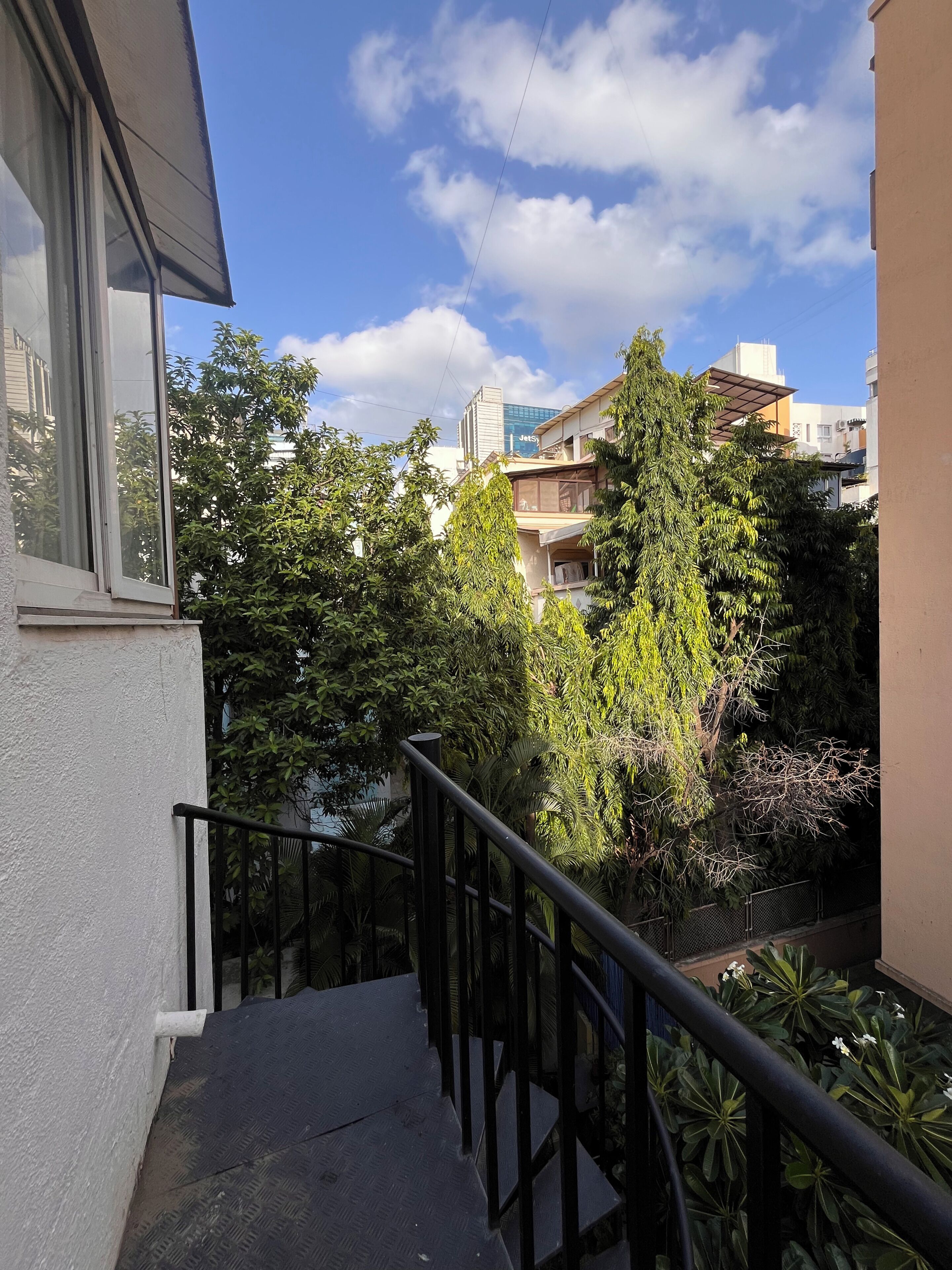Ein Wohngebäude mit einer Treppe, die zu einem Balkon führt, umgeben von Bäumen und weiteren Gebäuden.