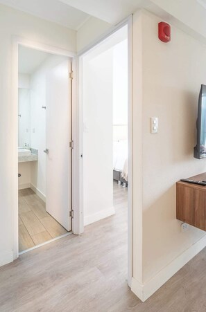 Une pièce avec un plancher en bois, un téléviseur fixé au mur et un détecteur d’incendie rouge.