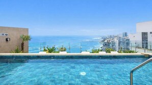 A clear blue pool with a view of the ocean and cityscape. - Sight 1601 · Luxe King Bed 1BR •Rooftop Pool, Gym, AC & Parking (Lima)