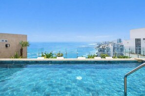 Ein klares, blaues Schwimmbecken mit Blick auf das Meer und die Stadtlandschaft.