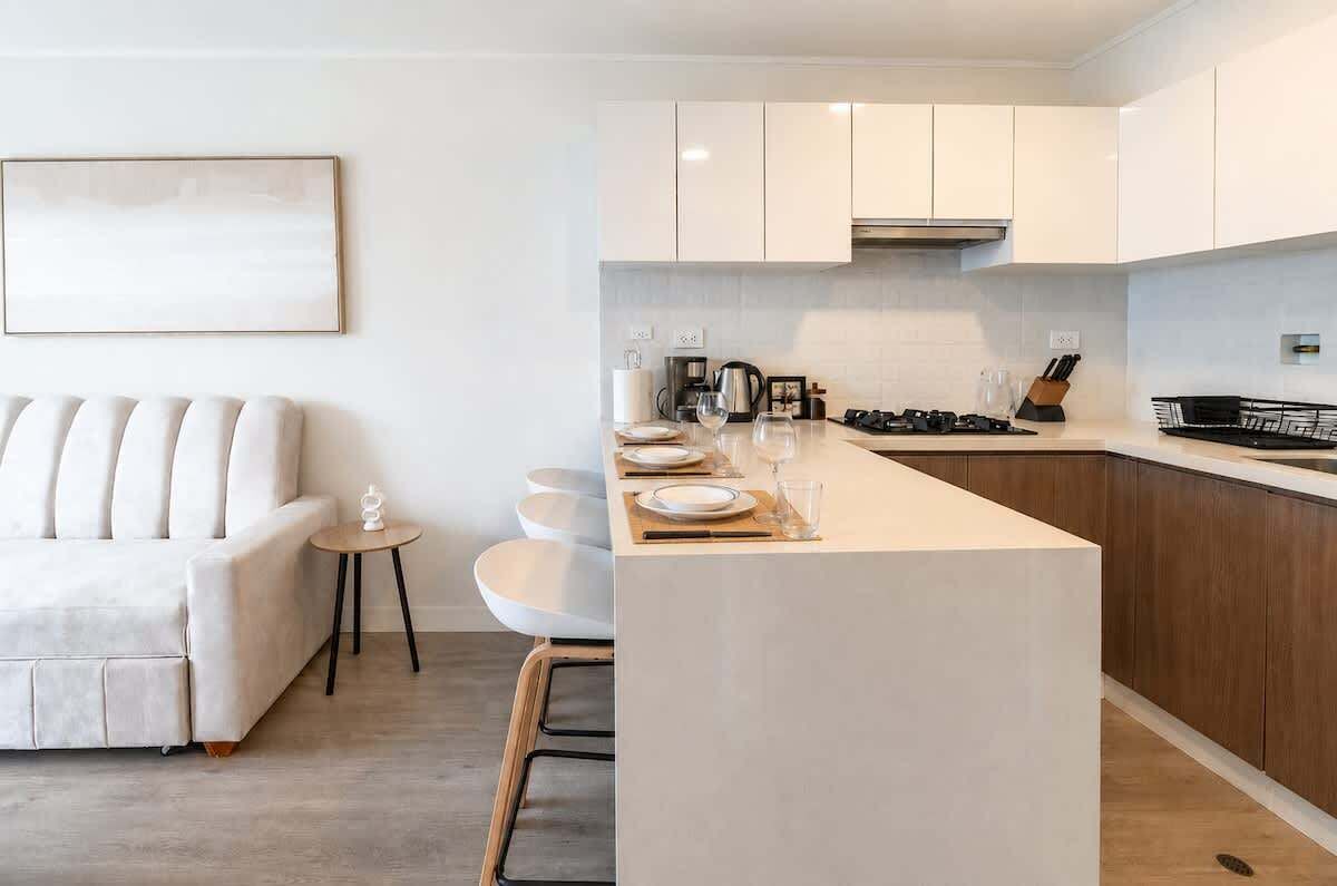 A modern kitchen with a central island, white cabinetry, and a sofa in the adjacent living area.