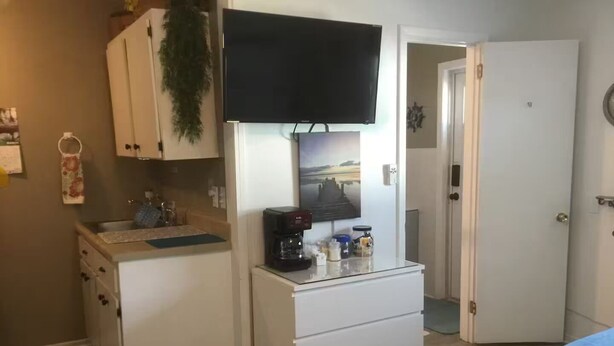 A compact room with a kitchenette, a flat-screen TV mounted above the counter, and a door leading to another room. - Charming 1-bedroom studio near Venice Beach (Venice)