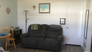 A room with a dark-colored sofa, a small wooden chair, a desk with a chair, a floor lamp, and a door. - Charming 1-bedroom studio near Venice Beach (Venice)