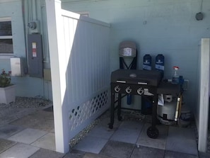 Ein Terrassenbereich mit Grill, Wasserspender und Mülleimer.