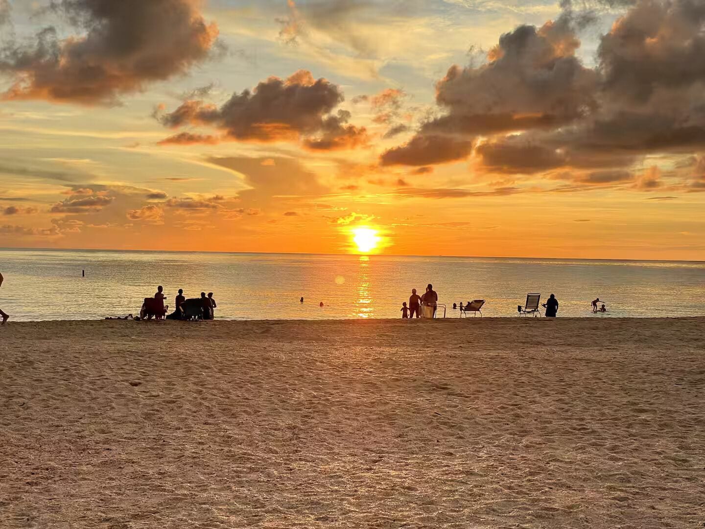 Une scène de plage au coucher du soleil, avec des silhouettes de personnes et de chaises de plage.