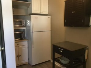 Une cuisine compacte avec un réfrigérateur blanc, un four à micro-ondes et une petite table sur laquelle se trouve un bol.