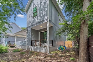 A two-story house with a covered porch, a wooden deck, and a play area with tires.