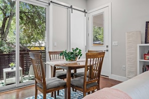 A room with a sliding glass door leading to a balcony, a wooden dining table with chairs, a potted plant, and a bookshelf.