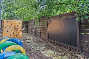 Ein umzäunter Spielbereich im Freien mit Kletterwand und Reckreifen.