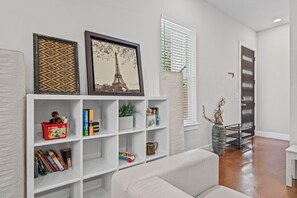 A modern living room with a white sofa, a bookshelf with various items, and a framed picture of the Eiffel Tower.
