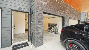 Un edificio moderno con una puerta de garaje, un felpudo y un coche estacionado afuera.